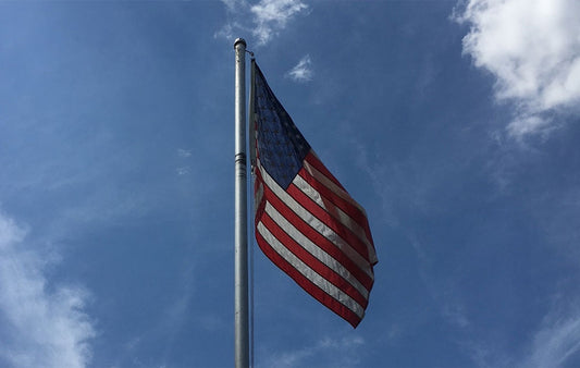 The flag of the United States on a flagpole with a blue sky in the basckground.