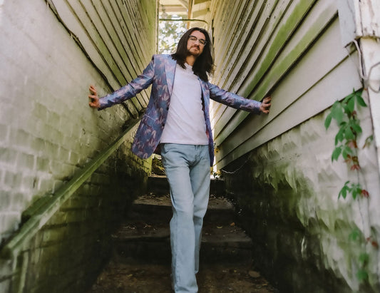 Man with long brown hair and glasses, standing on a stairway between two white walls.