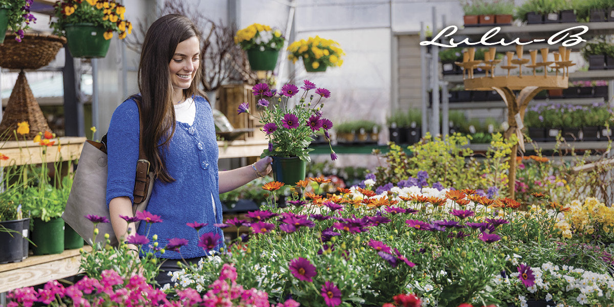 Woman wearing a Lulu‑B blue knit top holding flowers in a garden center.