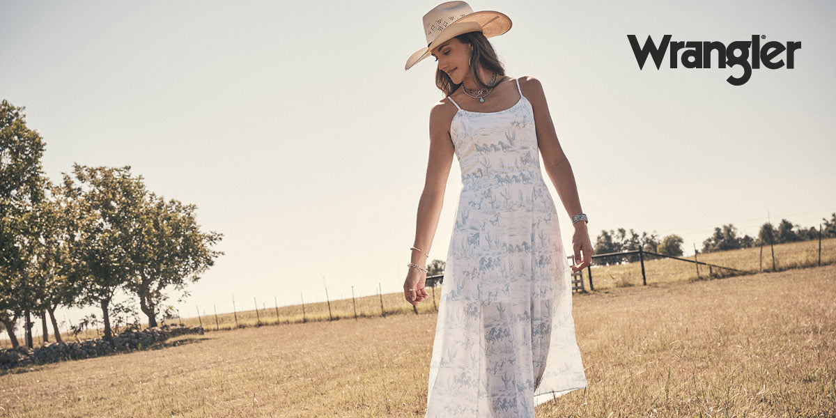 Woman standing in a field wearing a white Wrangler dress and hat.