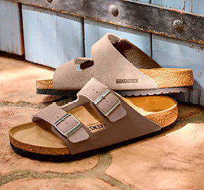 Pair of brown Birkenstock Arizona sandals against a blue background. 